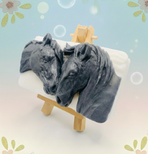 Load image into Gallery viewer, A grey and white handmade vegan soap featuring a highly detailed relief of two horses nuzzling heads, displayed on a wooden easel against a whimsical farmhouse decor background.
