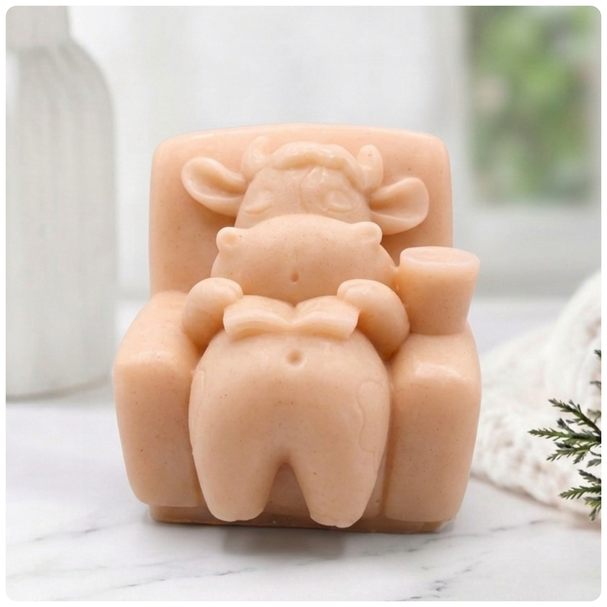 Handmade pink Lazy Cow soap sitting in an armchair reading a book with a candle, eyes closed in a relaxed pose. Unique decorative animal soap by Soap Simple Creations, Blackpool UK.