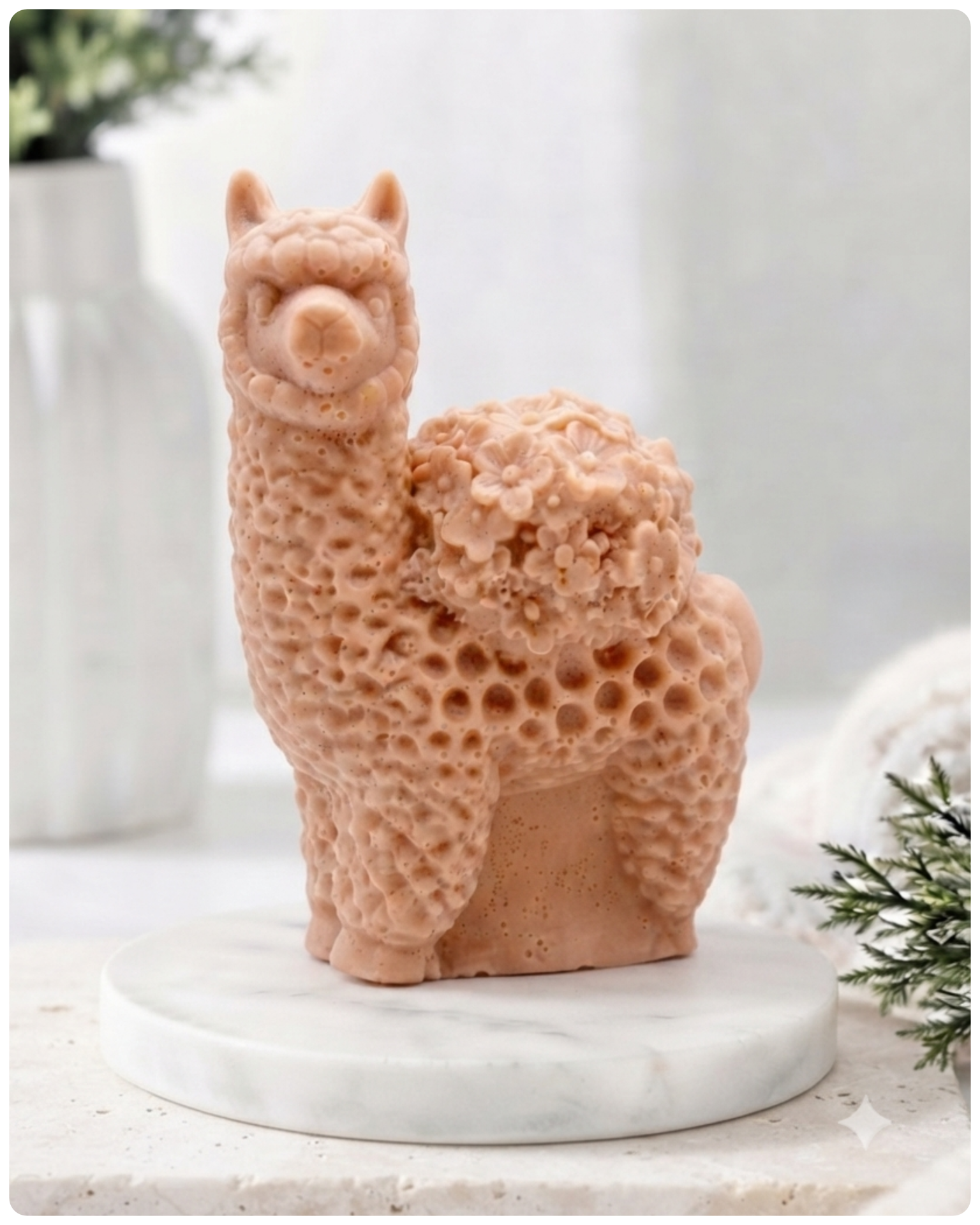 A handmade vegan soap featuring a charming llama or alpaca with a highly textured, fleecy coat and a blanket of intricate flowers across its back, displayed on a light wooden surface in a bright room.