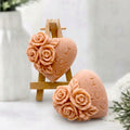 Two terracotta heart-shaped decorative soap bars engraved with 'I LOVE YOU' and 'I LOVE U', each adorned with raised rose details, displayed on a small wooden easel and beside one standing upright on a light surface with soft floral props.