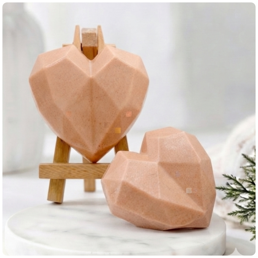 Two handmade vegan soaps in a contemporary geometric heart shape, with one displayed on a small wooden easel, set against a bright farmhouse decor background with white flowers.