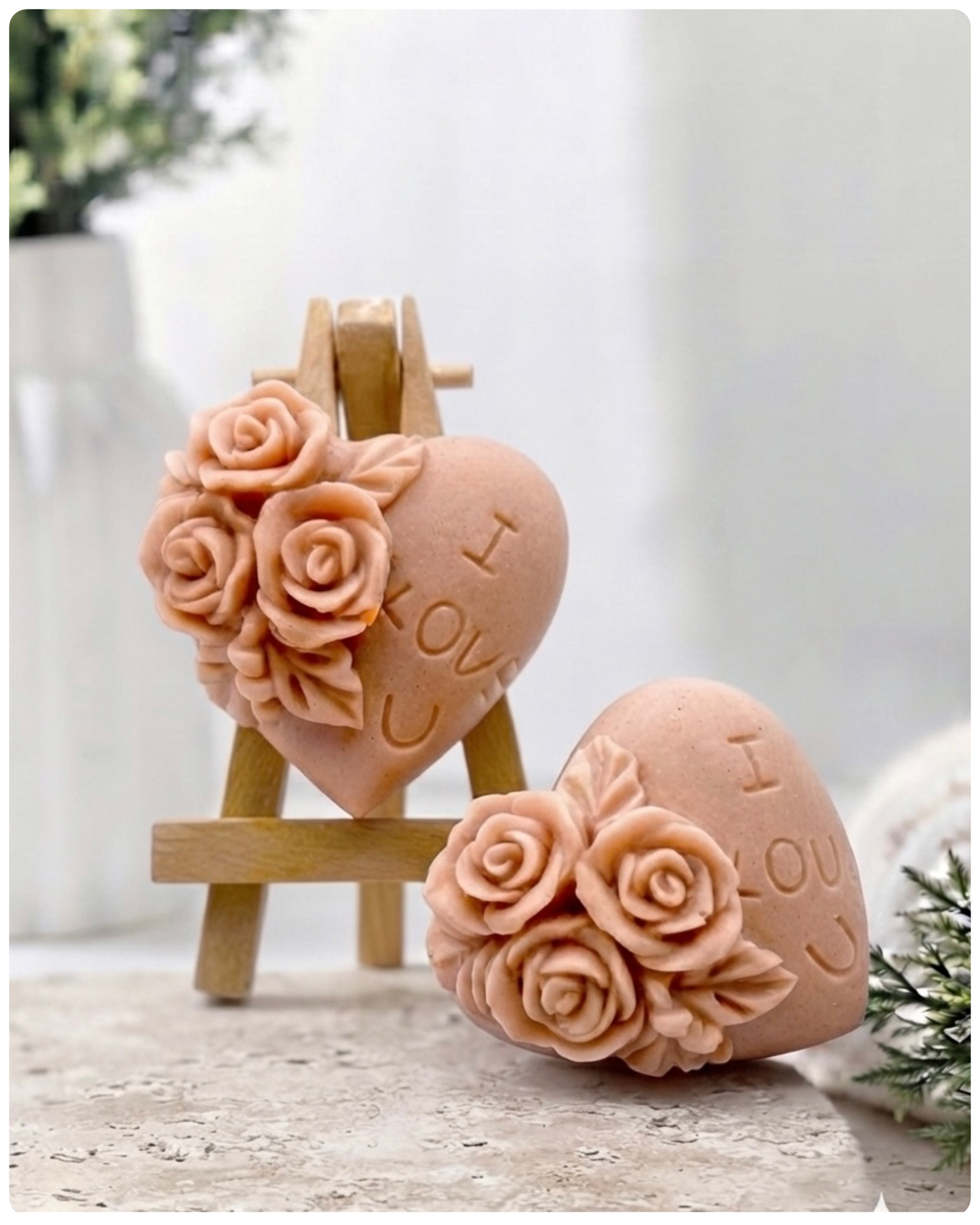 A handmade vegan soap gift set, featuring a central heart-shaped relief surrounded by a border of intricate rose flowers and delicate foliage, displayed on a small wooden easel.