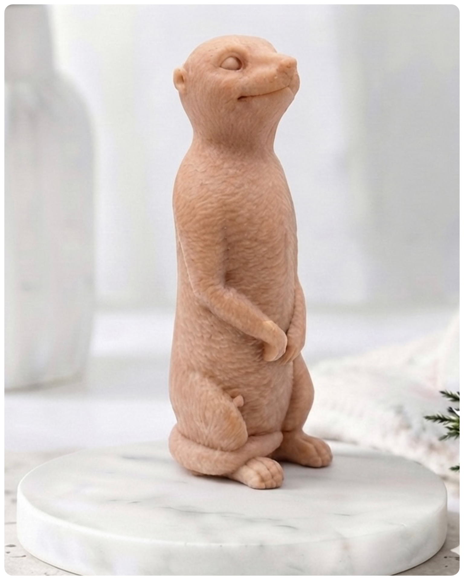 A highly detailed handmade vegan soap, sculpted in the shape of a realistic meerkat standing upright in its iconic sentinel pose, featuring textured fur and a curious facial expression, displayed on a light wooden surface.