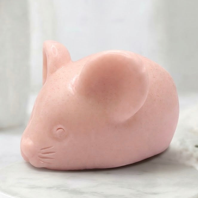 A soft pink handmade vegan soap sculpted into the shape of a cute resting mouse with large rounded ears and a delicate snout
