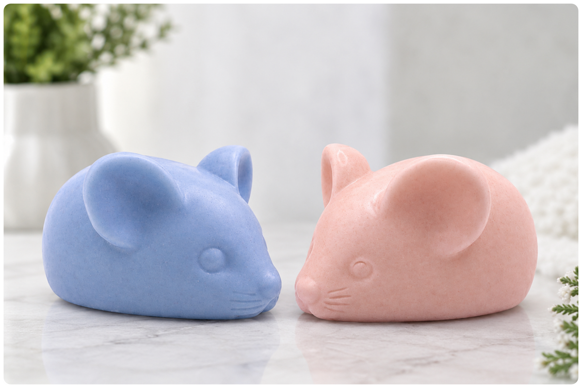 A close-up product photograph of two small, hand-sculpted artisan vegan mouse-shaped solid soaps, one light blue and one light rosy-pink by Soap Simple Creations, with large ears and whisker details, resting on a grey-veined marble surface. This image highlights the cruelty-free and plastic-free novelty gift range, handmade in Blackpool, England.