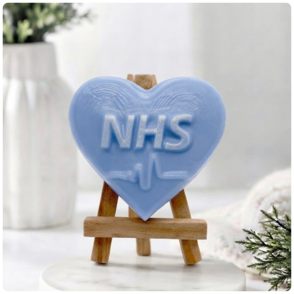 handmade vegan soap in a heart shape featuring an "NHS" relief and a heartbeat pulse line, displayed on a small wooden easel in a bright farmhouse decor setting.