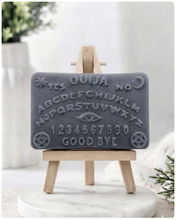 Load image into Gallery viewer, A rectangular handmade vegan soap featuring a highly detailed relief of a classic Ouija spirit board with the alphabet, numbers 0-9, an eye symbol, and the words "Yes," "No," and "Good Bye," displayed on a miniature wooden easel.
