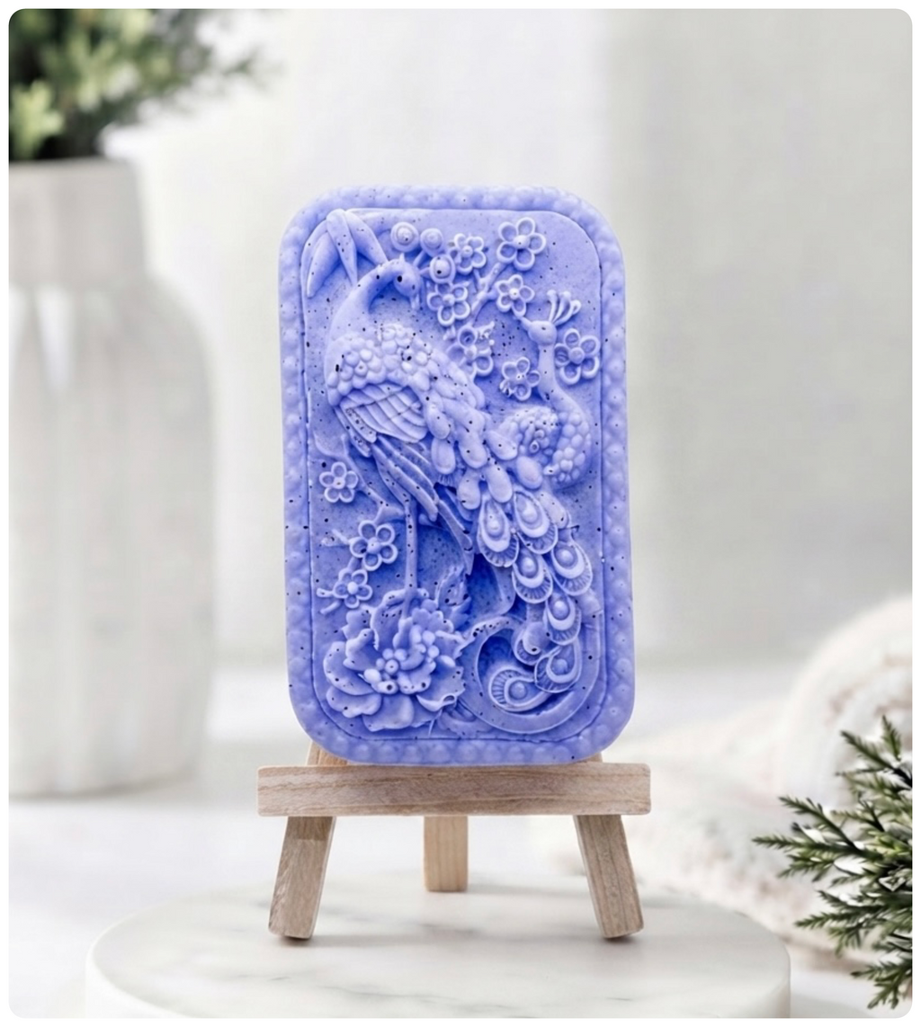 handmade vegan soap featuring a highly detailed relief carving of a peacock with a long, flowing tail, surrounded by delicate cherry blossoms and a large peony, displayed on a wooden easel.