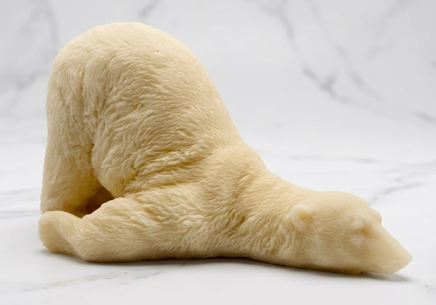 A yellow French clay bar of soap in the detailed form of a sleeping polar bear lying on its side, placed on white marble.