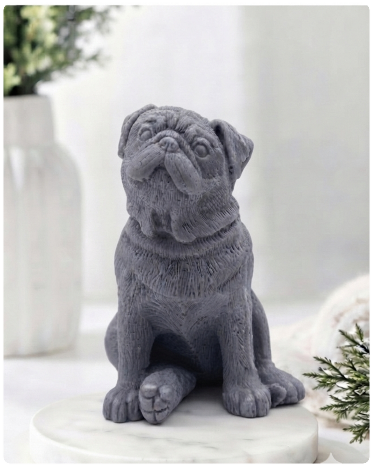 A detailed handmade vegan soap sculpted in the shape of a sitting pug dog with characteristic facial wrinkles and a tilted head, in a natural tone, displayed on a light wooden surface.