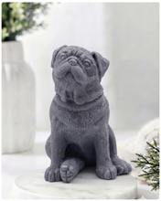 Load image into Gallery viewer, A detailed handmade vegan soap sculpted in the shape of a sitting pug dog with characteristic facial wrinkles and a tilted head, in a natural tone, displayed on a light wooden surface.
