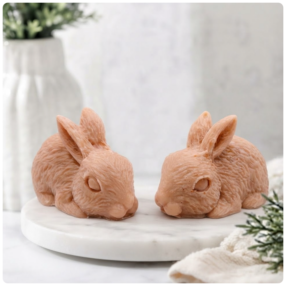 Two handmade rabbit soaps resting on a round marble tray against a neutral background.