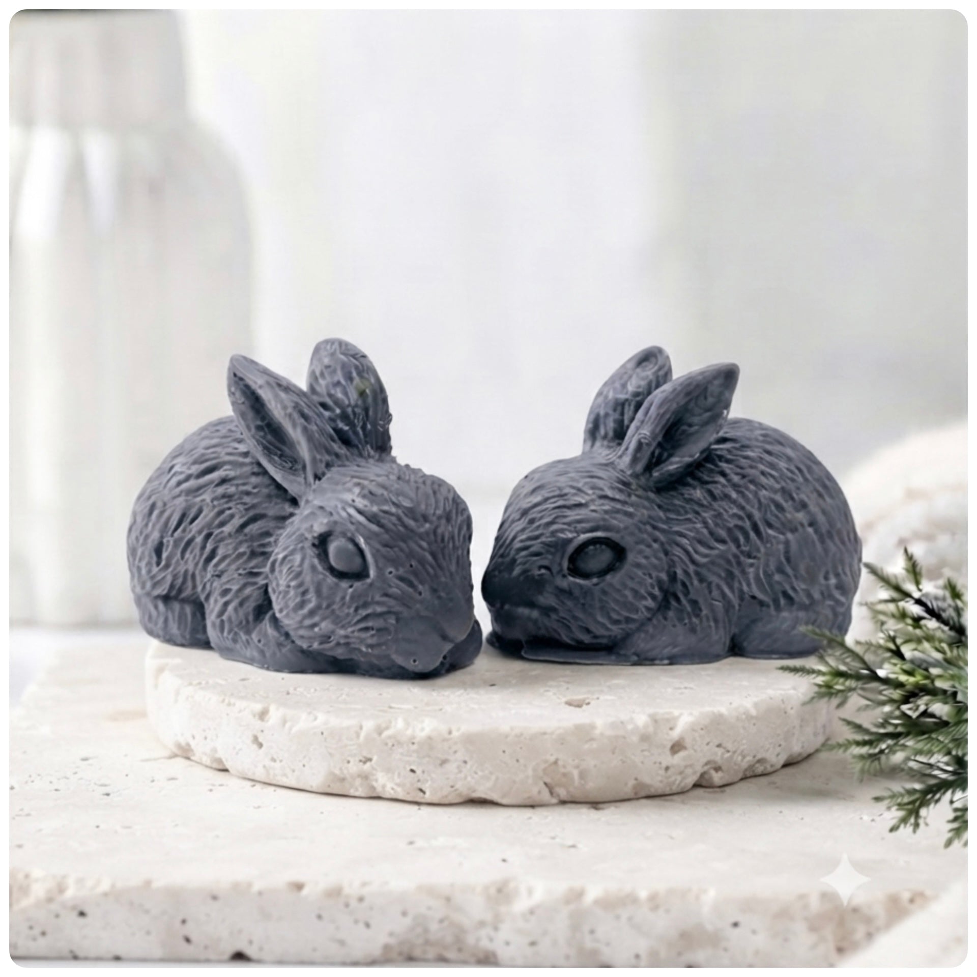 Set of two handmade vegan soaps in the shape of realistic crouching rabbits with detailed fur texture, displayed on a rustic white wooden surface in a bright farmhouse decor setting. Gift boxed. 