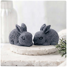 Load image into Gallery viewer, Set of two handmade vegan soaps in the shape of realistic crouching rabbits with detailed fur texture, displayed on a rustic white wooden surface in a bright farmhouse decor setting. Gift boxed. 
