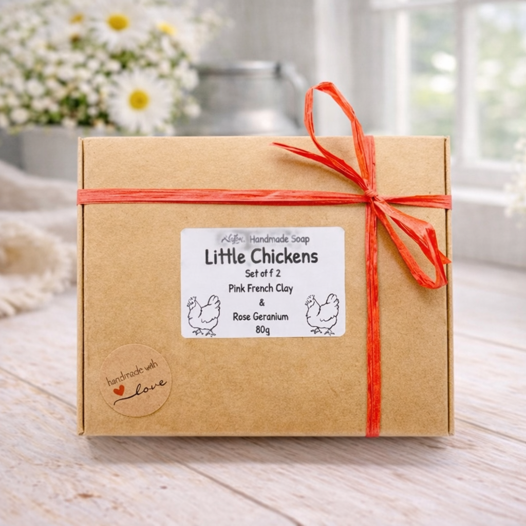 Two handmade vegan soaps in the shape of plump, realistic chicken sculptures with detailed feather textures, displayed on a rustic white wooden surface in a bright farmhouse decor setting.