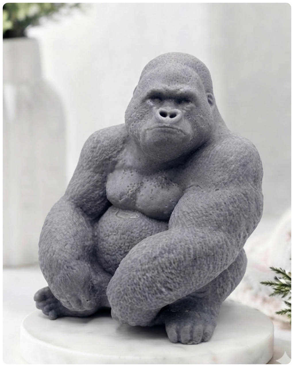 A large gray gorilla handmade soap sitting on a white marble base, photographed in a softly styled indoor setting with blurred decor in the background.