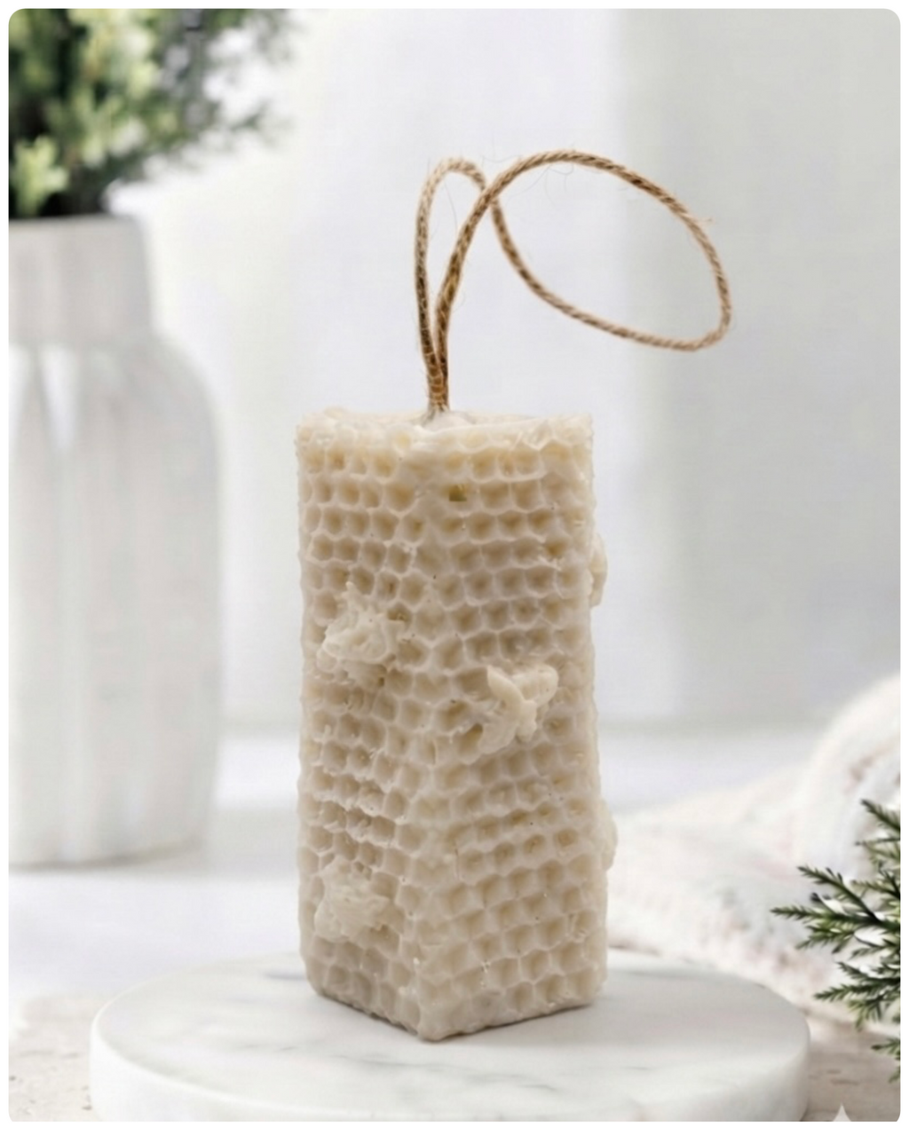 A tall, rectangular handmade vegan soap with a detailed honeycomb texture on all sides and small embossed bees, featuring a natural twine hanging rope, displayed upright on a light wooden surface.