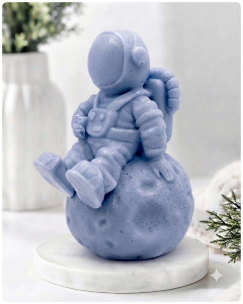 handmade vegan soap in the shape of a realistic astronaut sculpture sitting on the moon, featuring detailed spacesuit textures and craters on the lunar surface, displayed in a bright farmhouse decor setting.