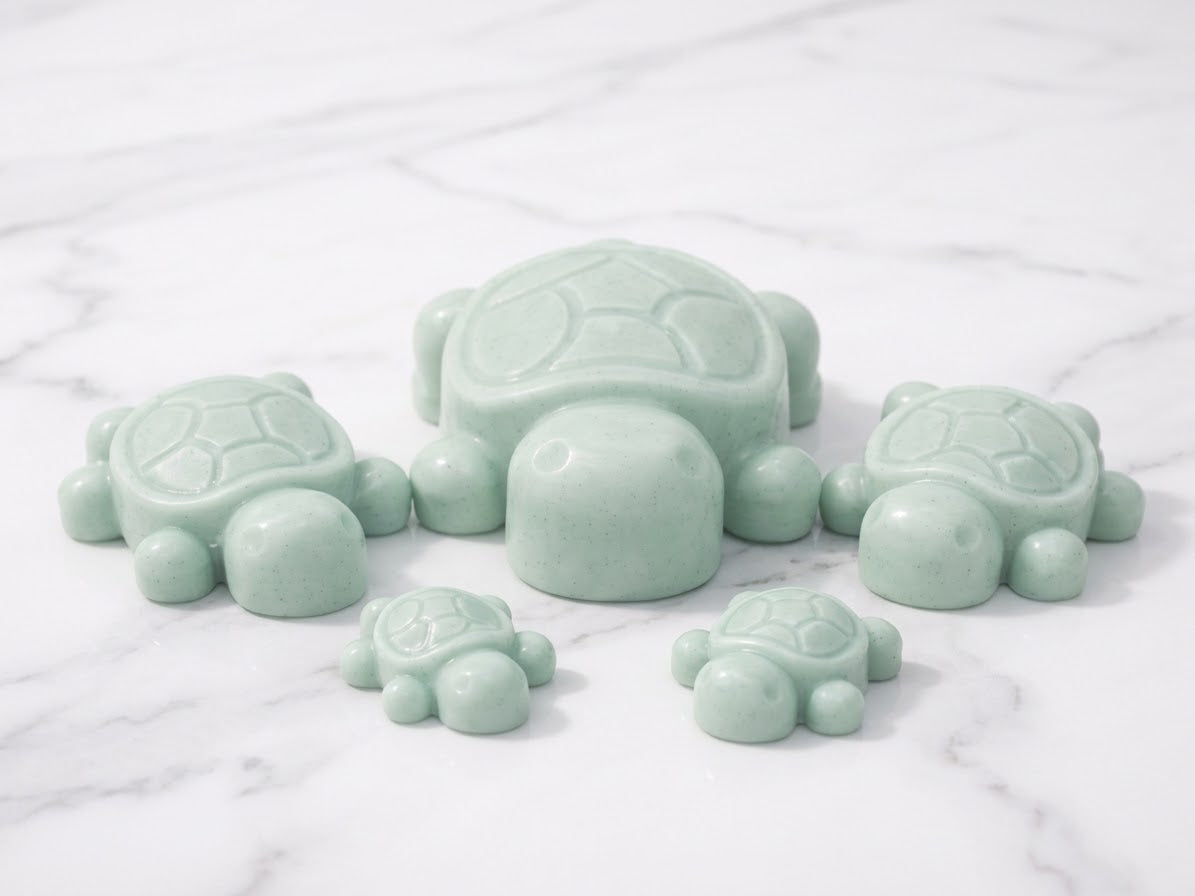 A family-themed cluster of five pale mint-green coloured artisan turtle soap bars, including one large and two smaller pairs, resting on a white marble countertop. Unique natural ingredient soap gift set.