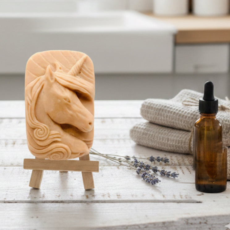 handmade vegan soap featuring a detailed unicorn head relief with a spiralled horn and flowing curly mane, displayed on a small wooden easel in a bright farmhouse decor setting.