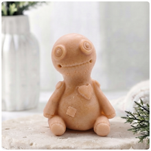 Load image into Gallery viewer, A handmade vegan soap gift in the shape of a stitched voodoo doll with button eyes and a small patch on its chest, sitting on a light wooden surface.
