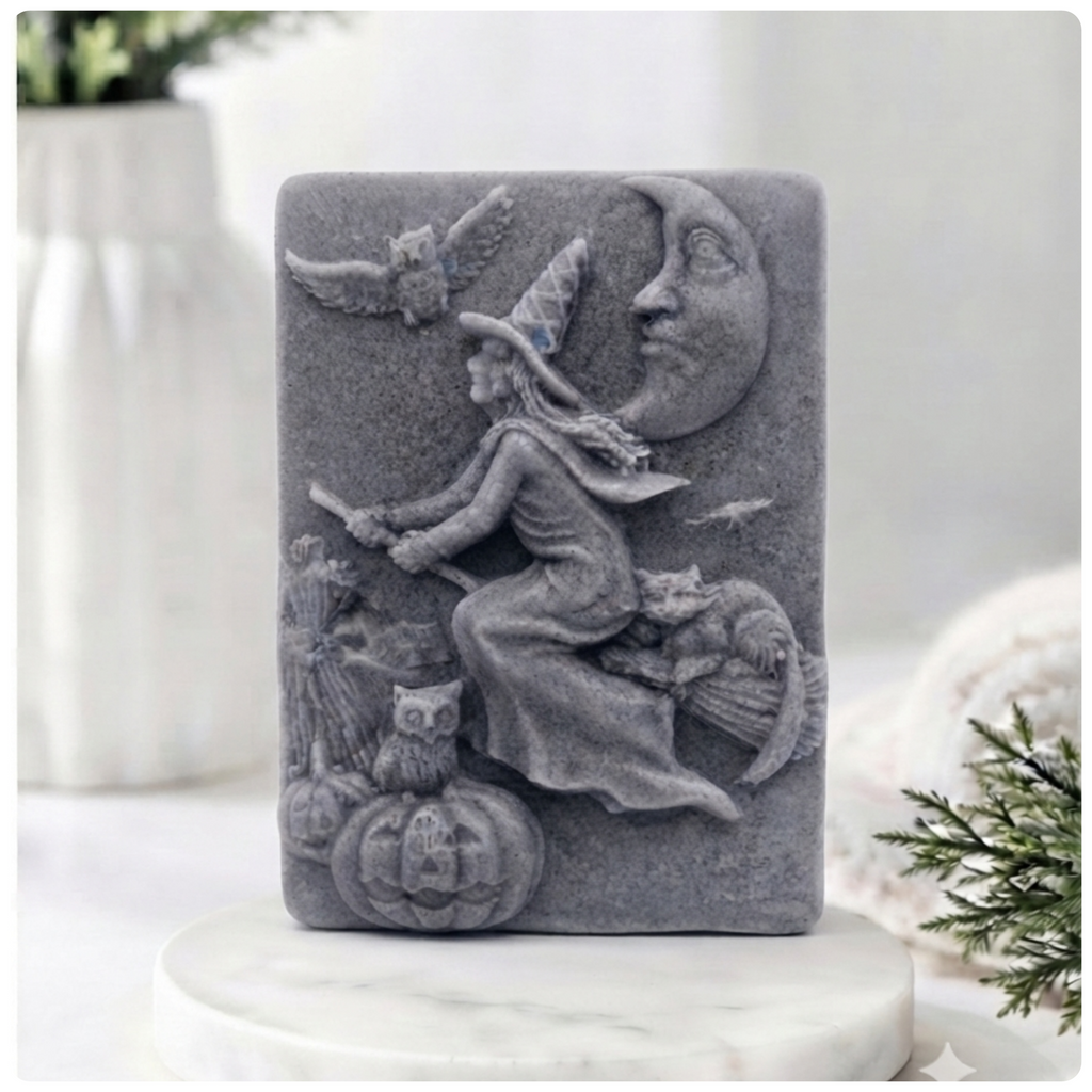 handmade vegan soap bar featuring a detailed relief carving of a witch flying on a broomstick past a crescent moon, owls, and pumpkins.