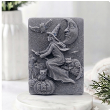 Load image into Gallery viewer, handmade vegan soap bar featuring a detailed relief carving of a witch flying on a broomstick past a crescent moon, owls, and pumpkins.
