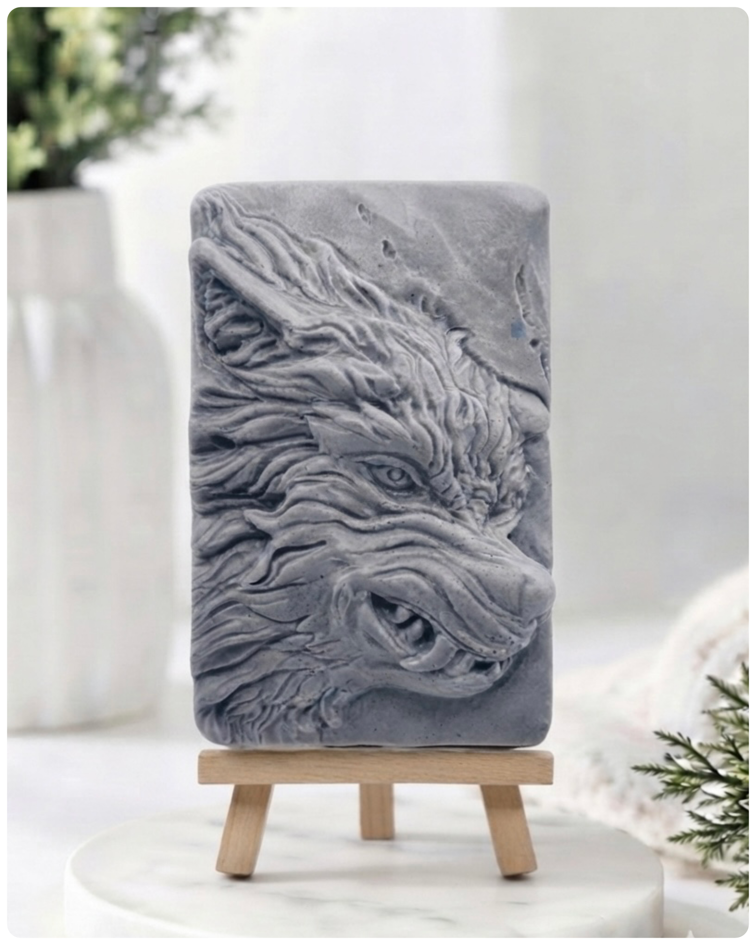 A rectangular handmade vegan soap featuring a highly detailed, 3D relief carving of a wolf's head in profile with a thick, textured mane, displayed on a miniature wooden easel.