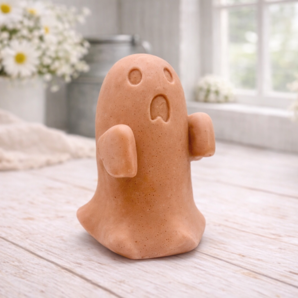 Handmade vegan soap ghost gift with a surprised expression, displayed on a light timber surface with soft white daisies in the background.