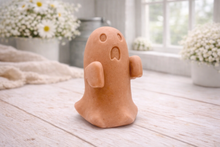 Load image into Gallery viewer, Handmade vegan soap ghost gift with a surprised expression, displayed on a light timber surface with soft white daisies in the background.
