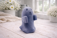 Load image into Gallery viewer, Handmade vegan soap ghost gift with a surprised expression, displayed on a light timber surface with soft white daisies in the background.
