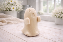 Load image into Gallery viewer, Handmade vegan soap ghost gift with a surprised expression, displayed on a light timber surface with soft white daisies in the background.
