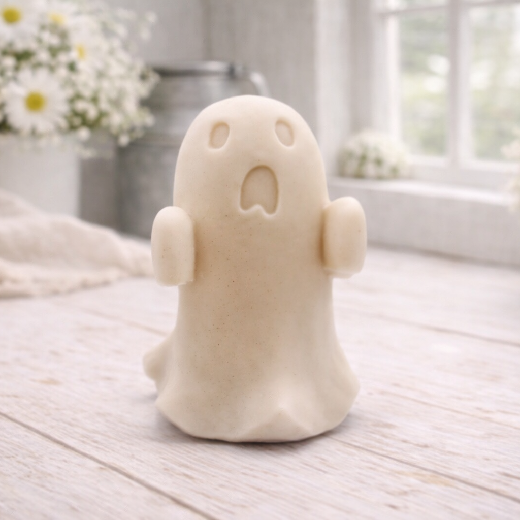 Handmade vegan soap ghost gift with a surprised expression, displayed on a light timber surface with soft white daisies in the background.