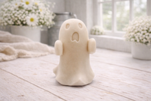 Load image into Gallery viewer, Handmade vegan soap ghost gift with a surprised expression, displayed on a light timber surface with soft white daisies in the background.
