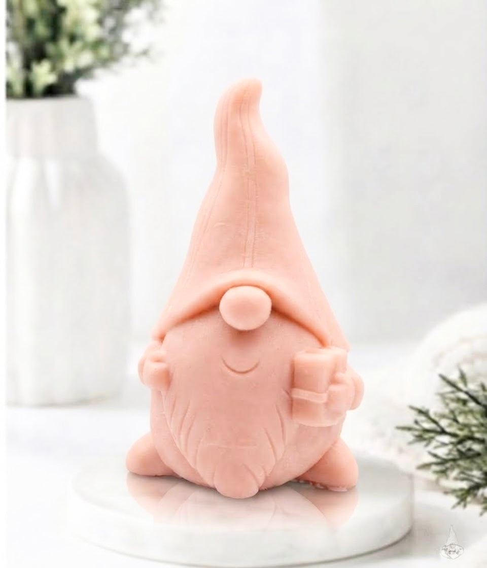 Front view of a soft pink gnome-shaped soap bar holding a small present on a marble display.