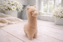 Load image into Gallery viewer, handmade vegan soap in the shape of a realistic standing alpaca sculpture, featuring detailed curly wool texture and a smiling face, displayed on a rustic white wooden surface in a bright farmhouse decor setting.

