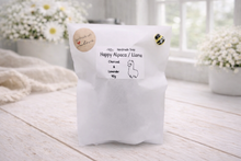 Load image into Gallery viewer, handmade vegan soap in the shape of a realistic standing alpaca sculpture, featuring detailed curly wool texture and a smiling face, displayed on a rustic white wooden surface in a bright farmhouse decor setting.
