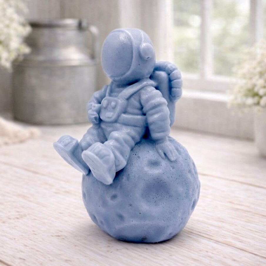 handmade vegan soap in the shape of a realistic astronaut sculpture sitting on the moon, featuring detailed spacesuit textures and craters on the lunar surface, displayed in a bright farmhouse decor setting.