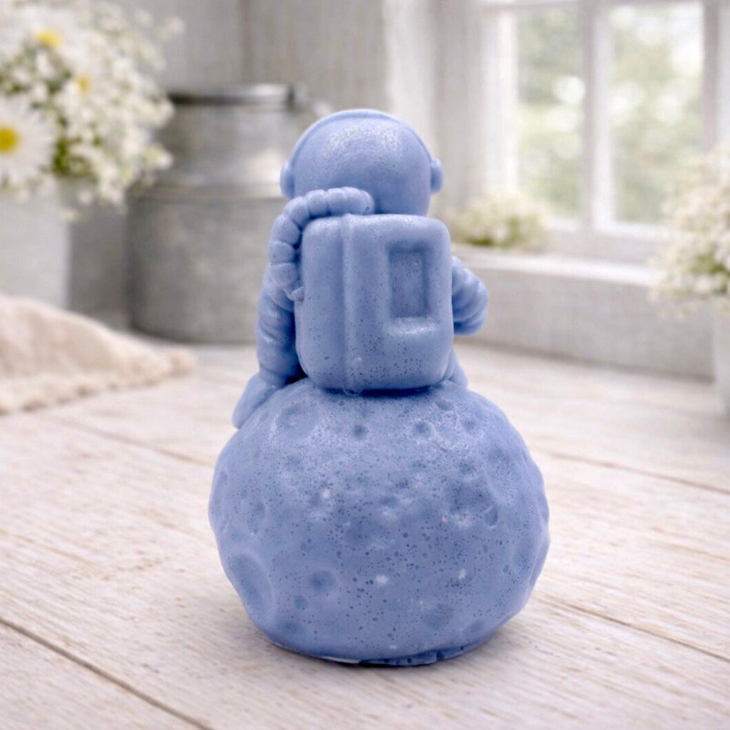 handmade vegan soap in the shape of a realistic astronaut sculpture sitting on the moon, featuring detailed spacesuit textures and craters on the lunar surface, displayed in a bright farmhouse decor setting.