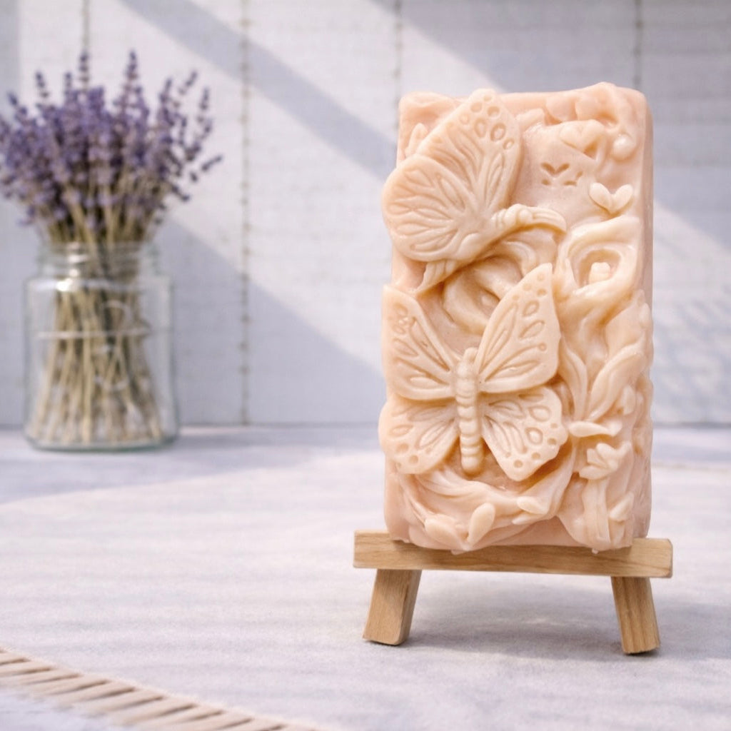 handmade vegan soap featuring a detailed 3D relief of butterflies and flowers, displayed on a wooden easel against a rustic farmhouse decor background with lavender.