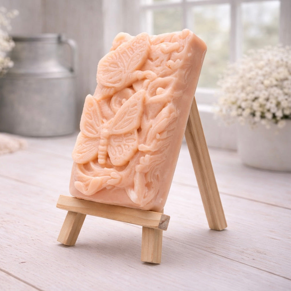 Decorative pink vegan soap with butterfly design on a small wooden easel in a bright room.