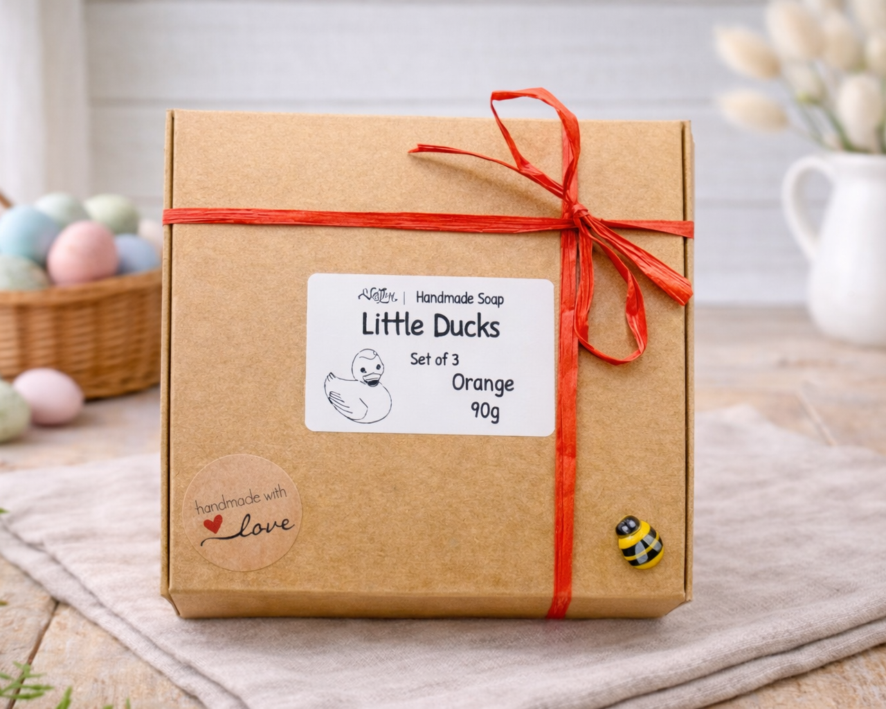 Gift box with 'Little Ducks' label and red ribbon on a wooden surface.