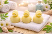 Load image into Gallery viewer, Three handmade vegan soaps in the shape of fluffy ducklings with open beaks, displayed on a neutral linen cloth in a bright farmhouse decor setting with Easter eggs in the background.
