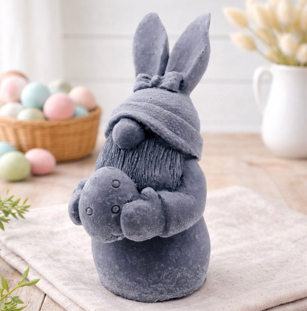 handmade vegan soap sculpture of a gnome wearing a rabbit-ear hat with a bow, holding a decorated Easter egg, set against a rustic background with a basket of pastel eggs.