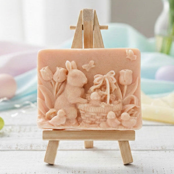 handmade vegan soap featuring a highly detailed 3D relief of a rabbit in a garden with tulips and an Easter basket, displayed on a wooden easel in a rustic farmhouse decor setting.