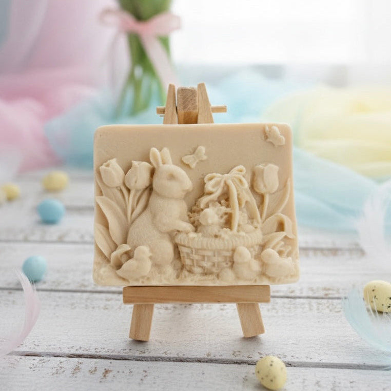 handmade vegan soap featuring a highly detailed 3D relief of a rabbit in a garden with tulips and an Easter basket, displayed on a wooden easel in a rustic farmhouse decor setting.