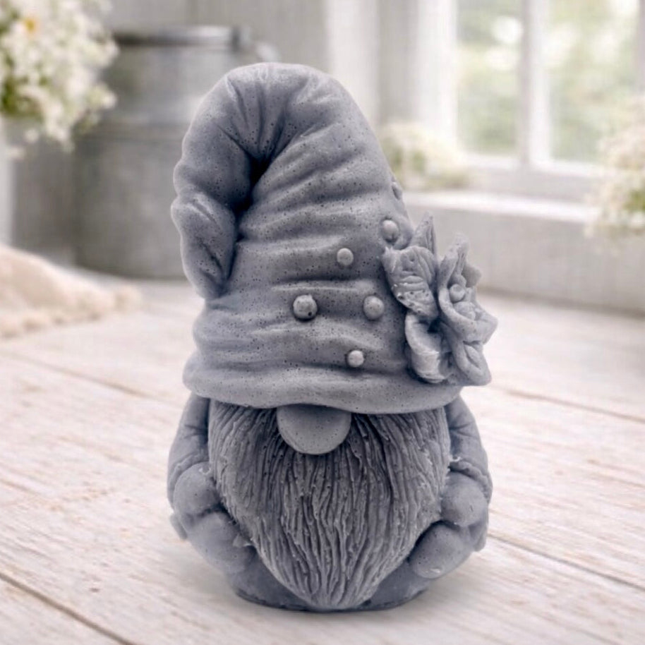 handmade vegan soap in the shape of a garden gnome sculpture with a long beard and a tall hat adorned with a large rose, displayed on a rustic white wooden surface in a bright farmhouse decor setting.