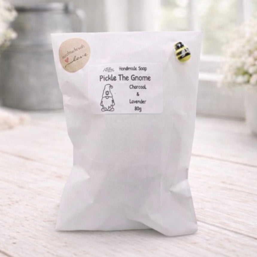 handmade vegan soap in the shape of a garden gnome sculpture with a long beard and a tall hat adorned with a large rose, displayed on a rustic white wooden surface in a bright farmhouse decor setting.