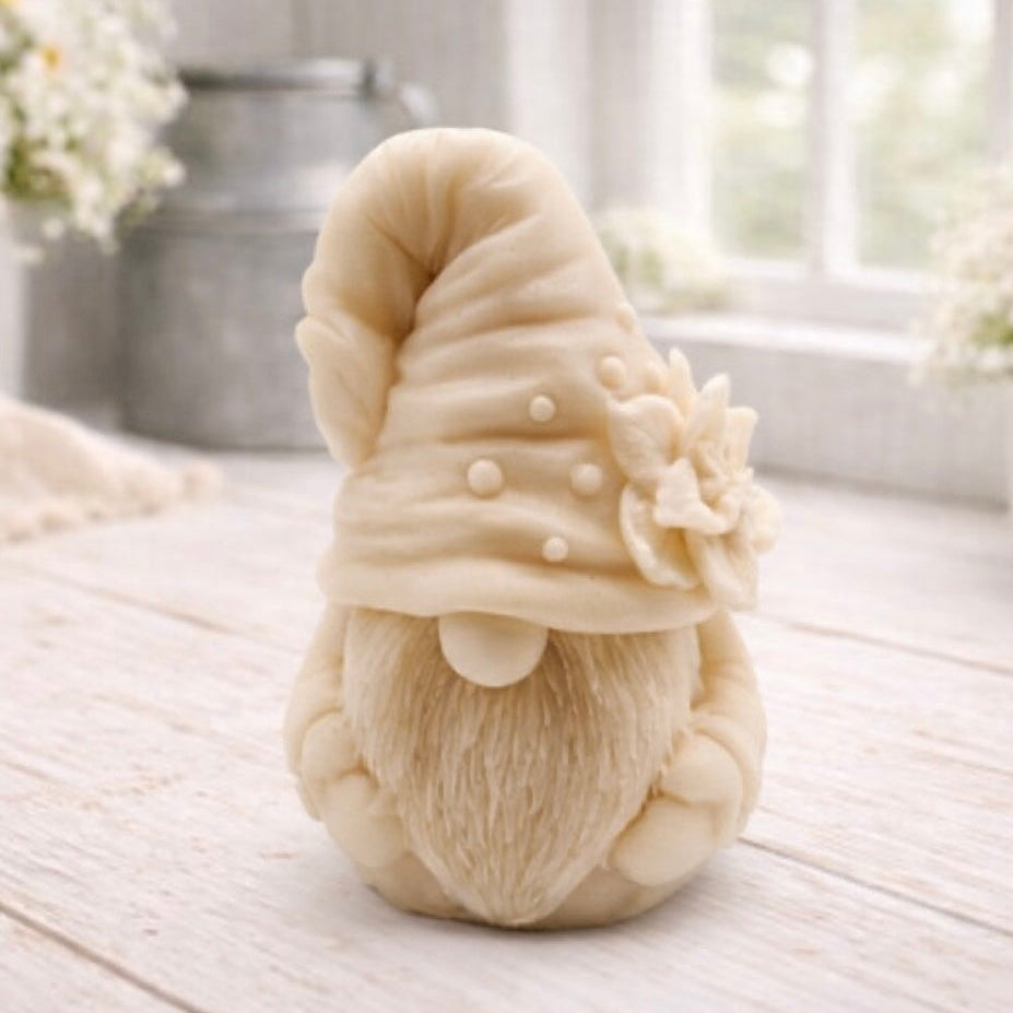 handmade vegan soap in the shape of a garden gnome sculpture with a long beard and a tall hat adorned with a large rose, displayed on a rustic white wooden surface in a bright farmhouse decor setting.
