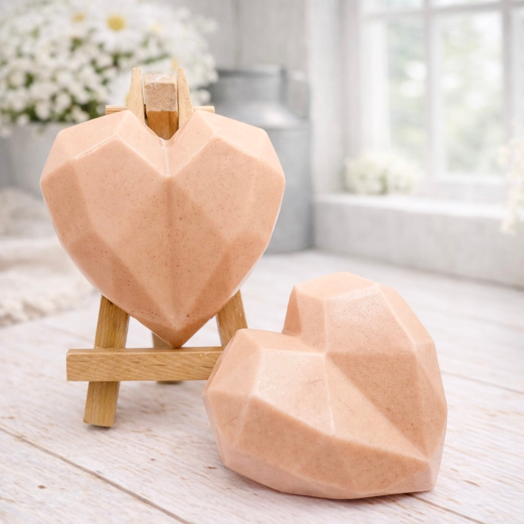 Two handmade vegan soaps in a contemporary geometric heart shape, with one displayed on a small wooden easel, set against a bright farmhouse decor background with white flowers.